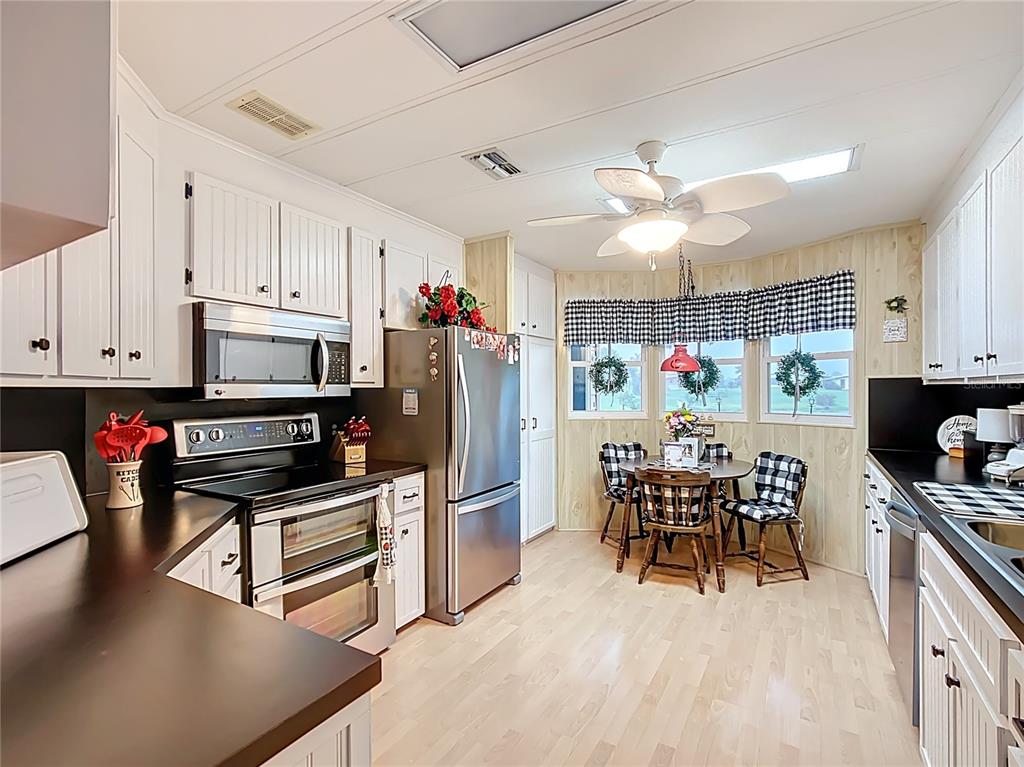 A kitchen features white cabinets, stainless steel appliances, a dining area, and light wood flooring — 6044 GRAND OAKS DRIVE SE, WINTER HAVEN, FL