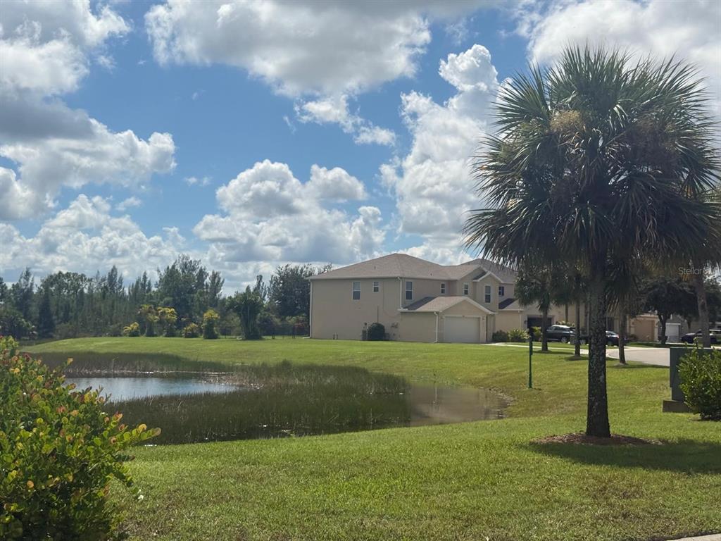 A two-story house sits behind a grassy lawn and a small pond under a cloudy sky — 18168 HORIZON VIEW BOULEVARD, LEHIGH ACRES, FL