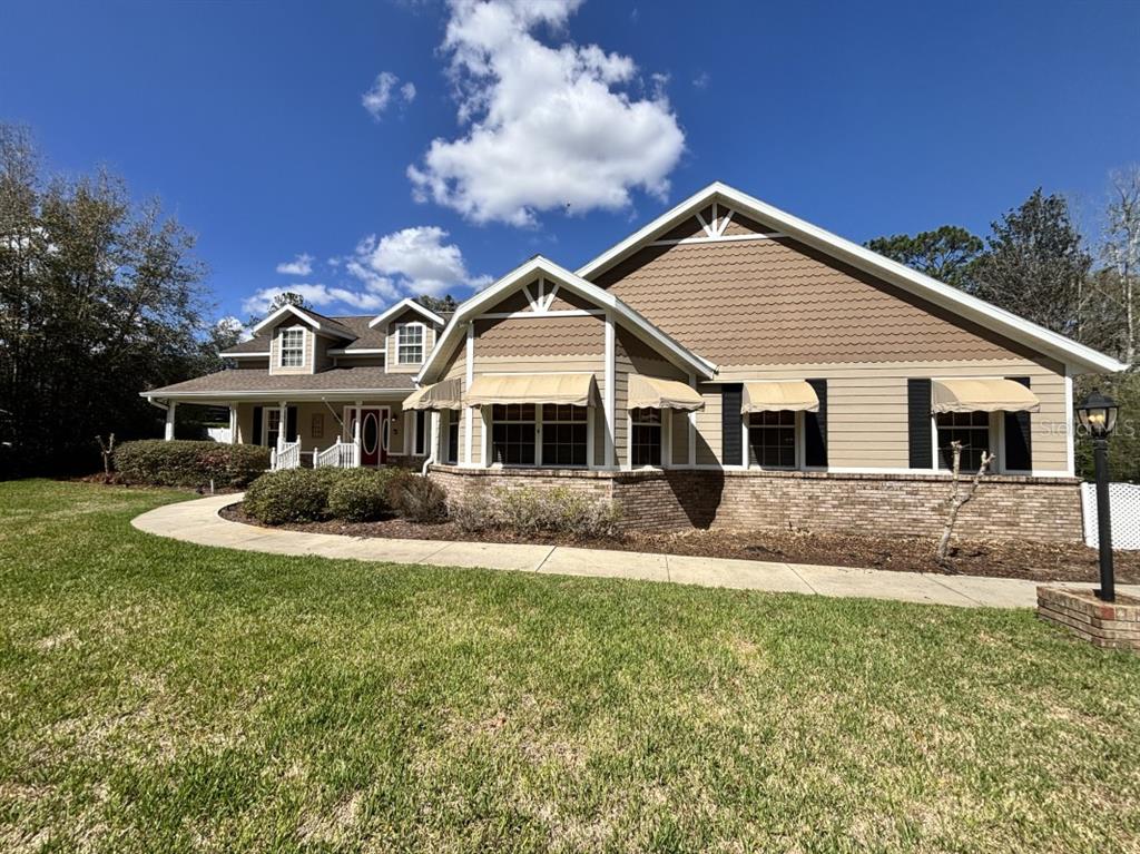 A tan, single-story house with a brick base, brown shingle siding, and beige window awnings — 1815 SE 89TH LANE, OCALA, FL