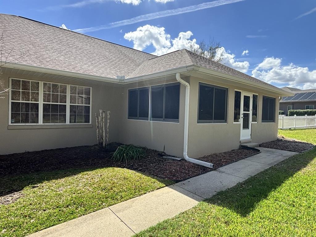 The exterior of a tan house features a screened-in porch, a white door, and a sidewalk — 1815 SE 89TH LANE, OCALA, FL