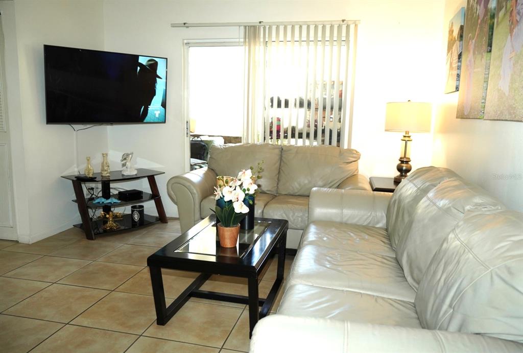 A living room features light-colored leather sofas, a glass-top coffee table, and a wall-mounted television — 1664 SUNNY BROOK LANE NE UNIT 103, PALM BAY, FL