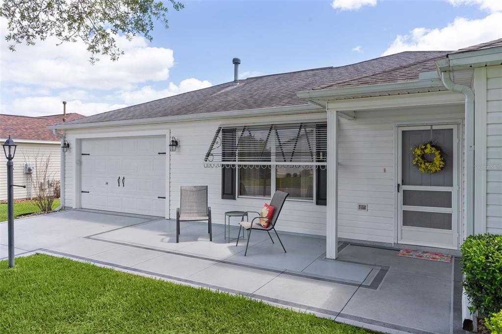 A white house exterior features a concrete patio, a garage, and a front entry door — 8015 SE 174TH BELHAVEN LOOP, THE VILLAGES, FL
