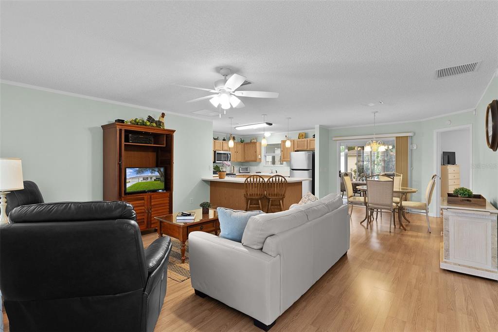 An open-concept living room and kitchen featuring light wood flooring and a ceiling fan — 8015 SE 174TH BELHAVEN LOOP, THE VILLAGES, FL