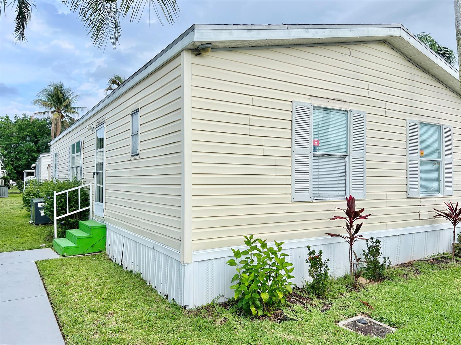 A light yellow mobile home with white skirting, green steps, and small landscaping plants — 183 Plantation Boulevard, Lake Worth FL 33467, LAKE WORTH, FL
