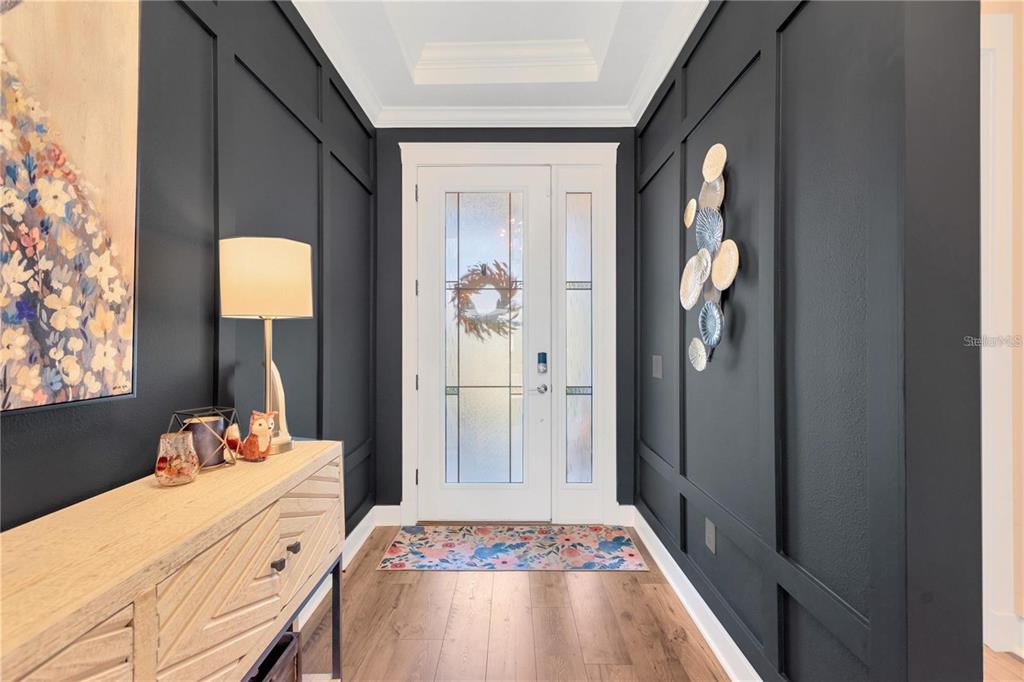 A foyer features dark paneled walls, a light wood console table, and a glass-paneled door — 7213 TALAMORE DRIVE, WESLEY CHAPEL, FL
