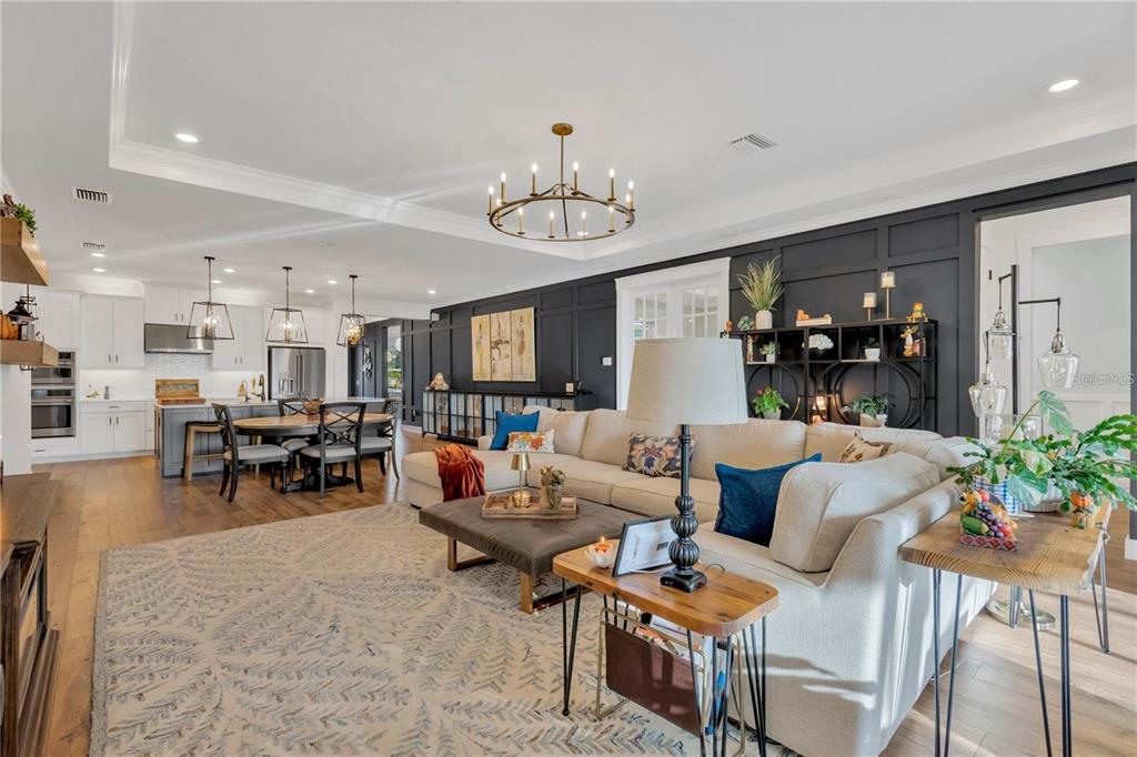 An open-concept living room and kitchen feature dark paneled walls, a large sectional, and chandeliers — 7213 TALAMORE DRIVE, WESLEY CHAPEL, FL