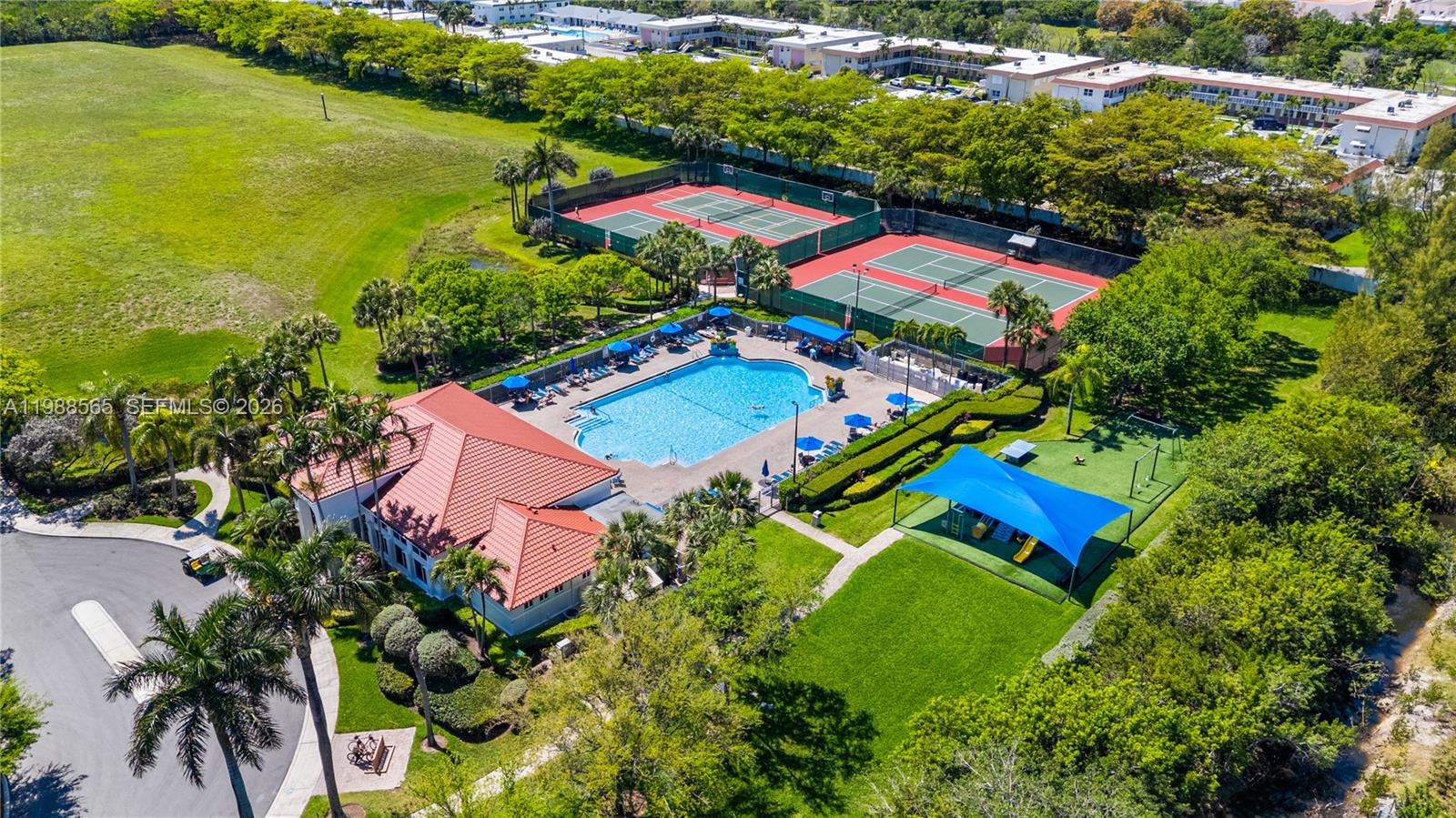 An aerial view shows a community clubhouse with a swimming pool, tennis courts, and playground — 1120 Canella Ln, Hollywood FL 33019, HOLLYWOOD, FL