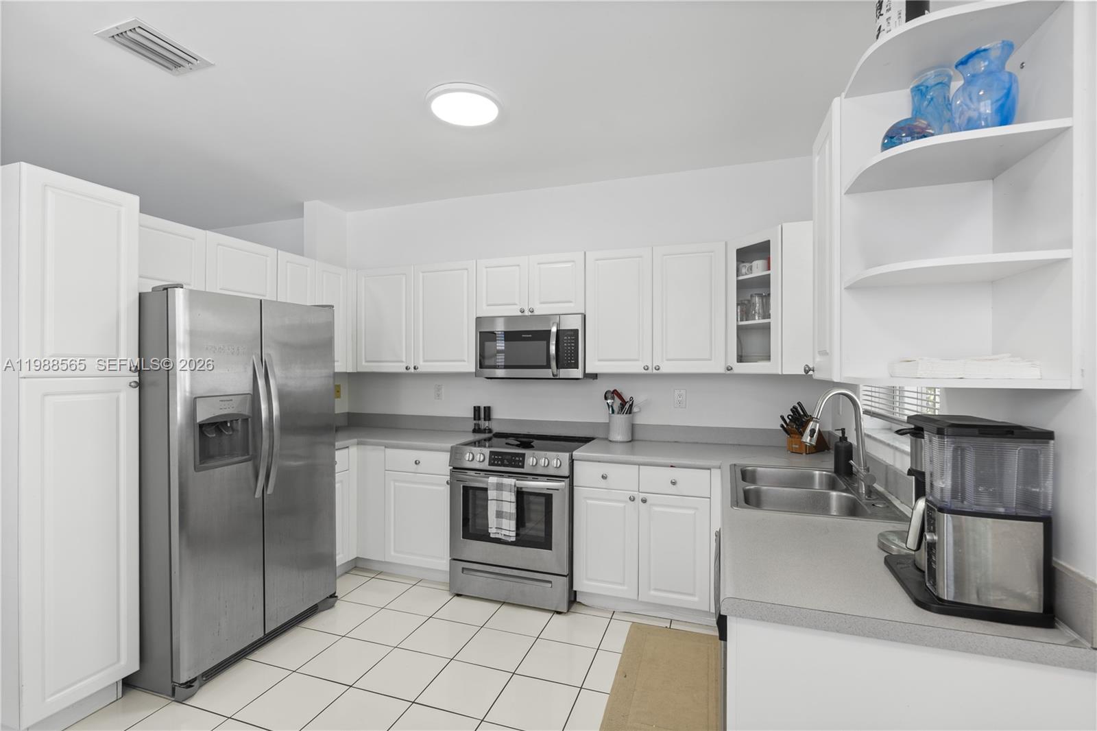 A kitchen features white cabinetry, stainless steel appliances, gray countertops, and white tile flooring — 1120 Canella Ln, Hollywood FL 33019, HOLLYWOOD, FL