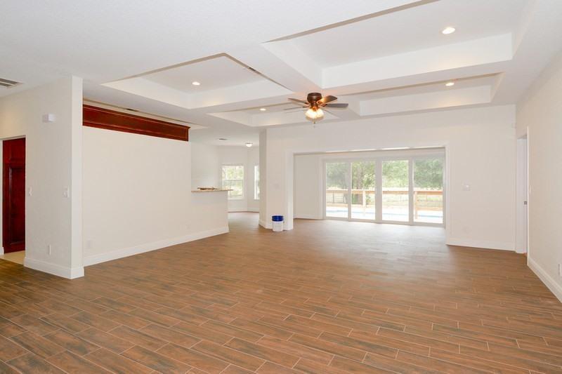 An open-concept living area features a tray ceiling, ceiling fan, and wood-look tile flooring — 4935 Lame Panther Lane, Loxahatchee FL 33470, LOXAHATCHEE, FL