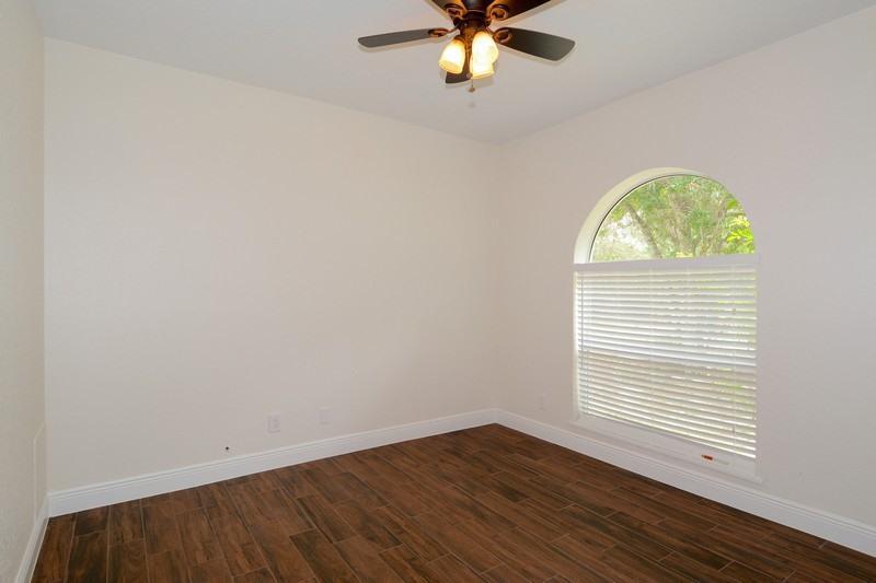 An empty bedroom features white walls, dark wood-look tile flooring, and an arched window — 4935 Lame Panther Lane, Loxahatchee FL 33470, LOXAHATCHEE, FL
