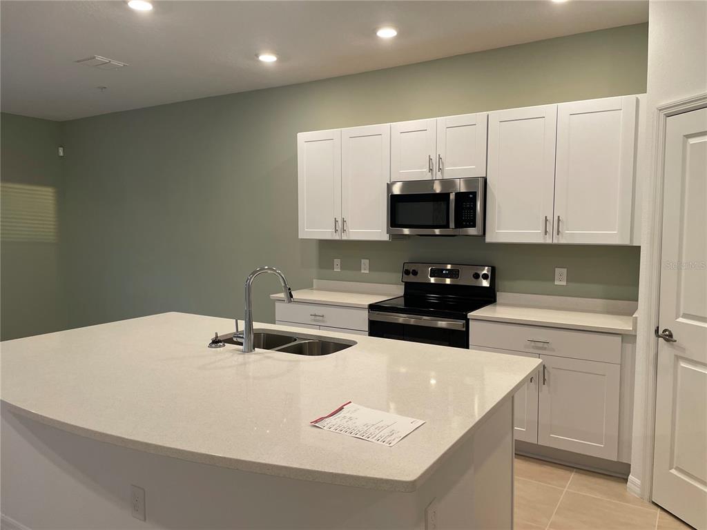 A kitchen features white cabinets, stainless steel appliances, a large island, and light-colored countertops — 4590 CALVARY WAY, ST CLOUD, FL