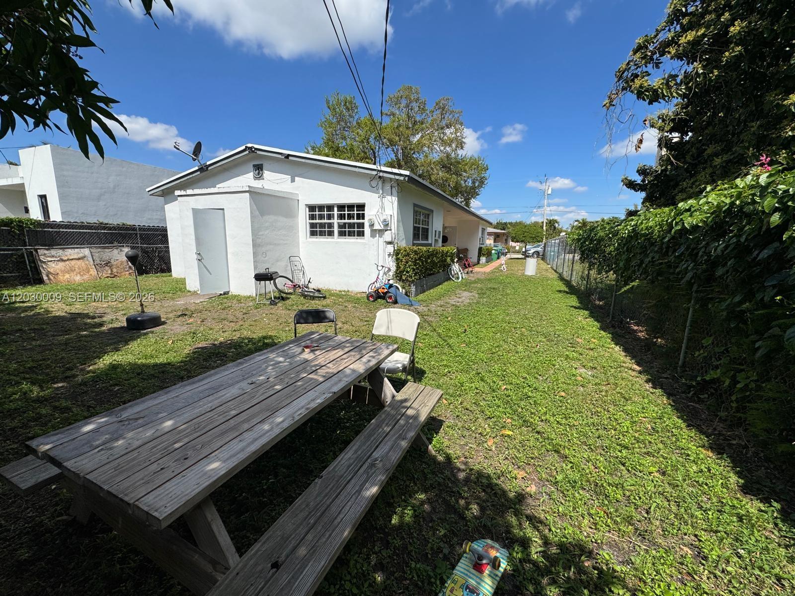 A white house with a wooden picnic table sits in a grassy backyard — 1226 NE 112th St # 1226, Miami FL 33161, MIAMI, FL