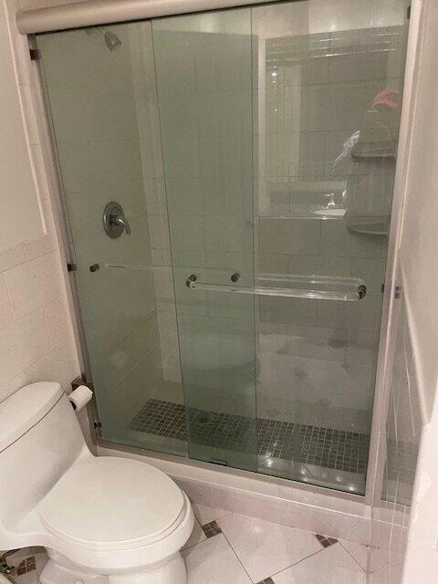 A bathroom features a tiled shower-tub combination with glass sliding doors and a white toilet — 6654 Via Regina, Boca Raton FL 33433, BOCA RATON, FL