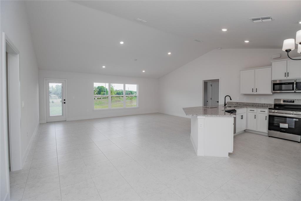 An open-concept kitchen and living area features white cabinets, granite countertops, and tile flooring — 1218 HICKORY NUT DRIVE, LAKE WALES, FL