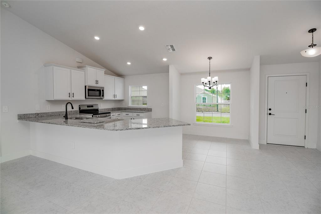 A kitchen with white cabinets, granite countertops, and tile flooring opens to a dining area — 1218 HICKORY NUT DRIVE, LAKE WALES, FL