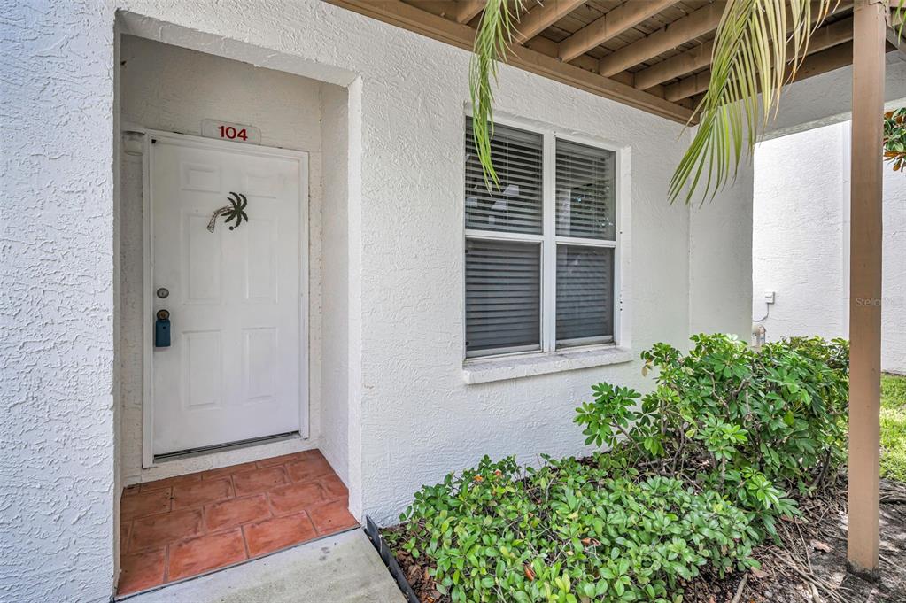 The exterior entrance of a white building features a door numbered 104 and landscaping — 1400 WATER VIEW DRIVE W UNIT 104, LARGO, FL