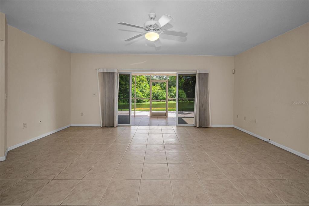 A spacious room with beige tile flooring, a ceiling fan, and sliding glass doors — 1400 WATER VIEW DRIVE W UNIT 104, LARGO, FL