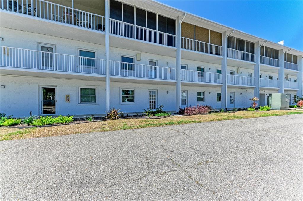 A three-story white apartment building with balconies and ground-level entrances faces a paved parking lot — 4920 38TH WAY S UNIT 210, ST PETERSBURG, FL