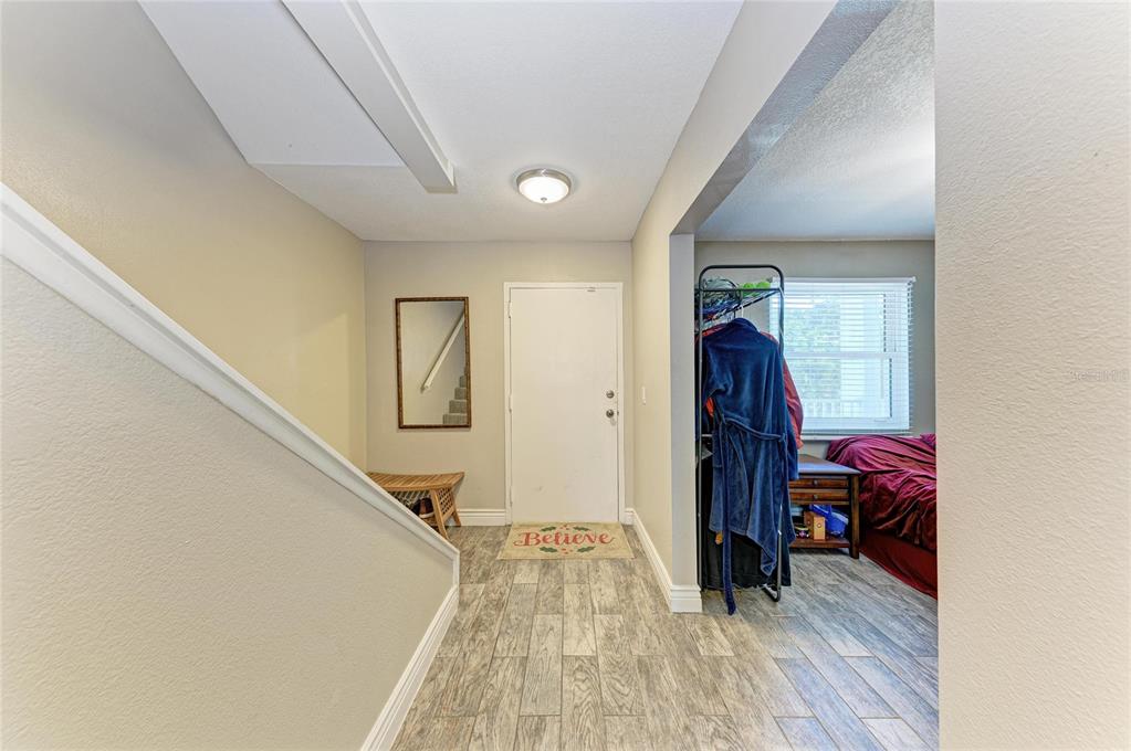 An entryway features wood-look tile flooring, a white front door, and a staircase railing — 4920 38TH WAY S UNIT 210, ST PETERSBURG, FL