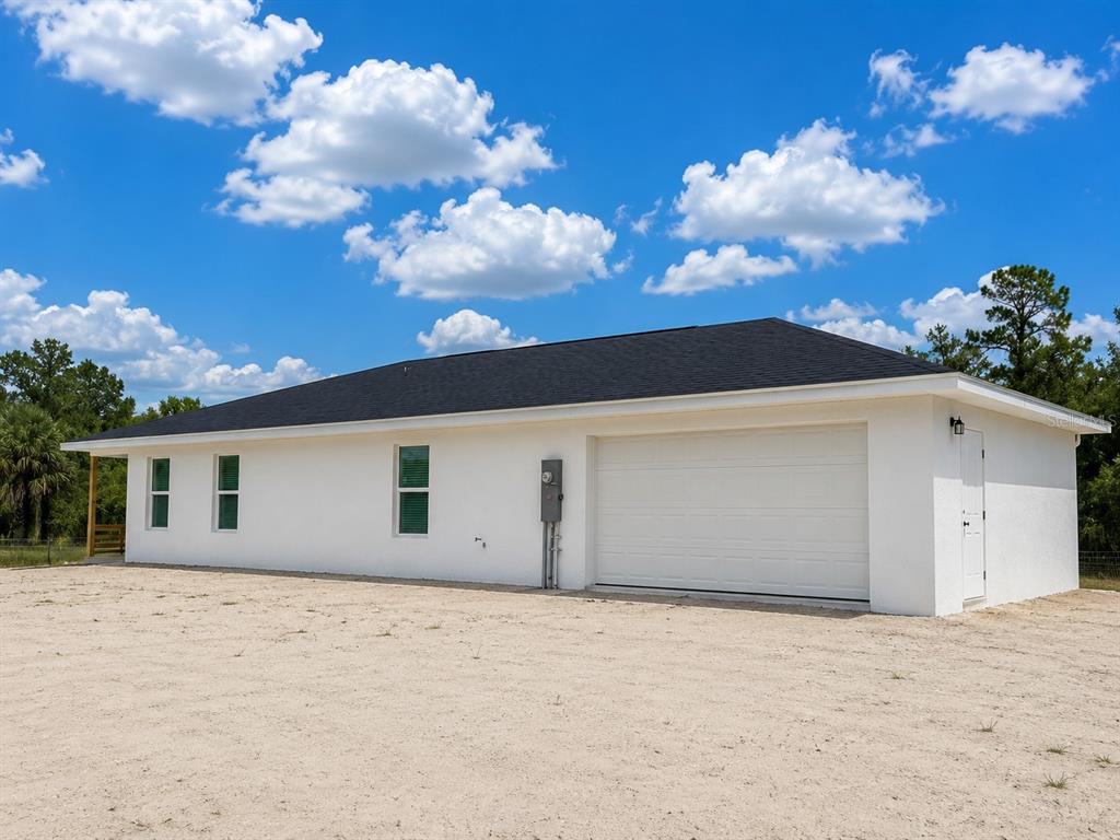 A white, single-story house exterior with a garage, a side door, and a gravel yard — 19570 NW 290TH STREET, OKEECHOBEE, FL