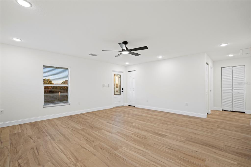 A bright, empty room features light wood-look flooring, white walls, a ceiling fan, and a door — 19570 NW 290TH STREET, OKEECHOBEE, FL