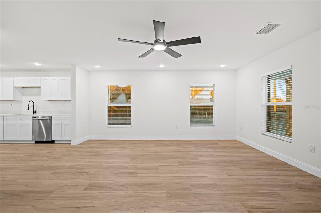 A bright, open-concept living area features light wood-look flooring, white cabinetry, and a ceiling fan — 19570 NW 290TH STREET, OKEECHOBEE, FL