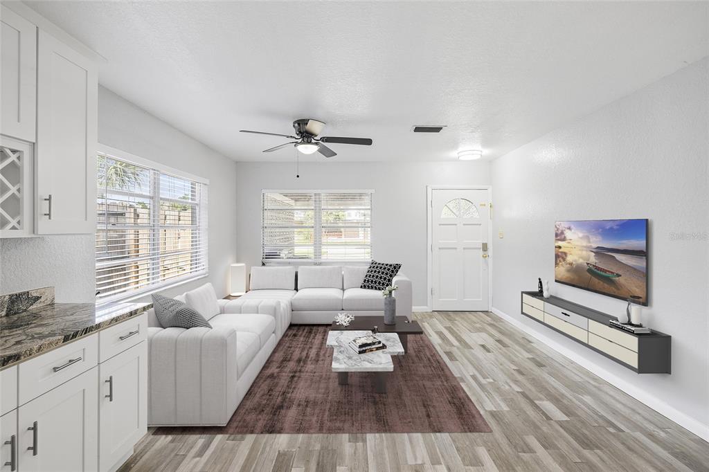 A bright living room features a white sectional sofa, a wall-mounted television, and wood-look flooring — 206 N GUNLOCK AVENUE, TAMPA, FL
