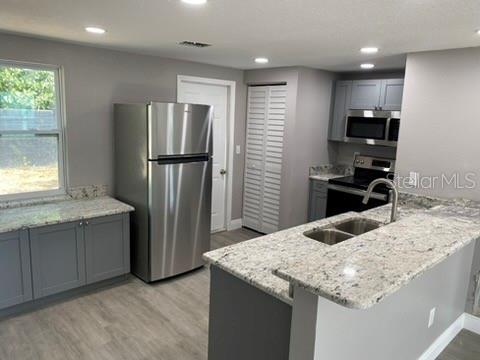 A kitchen features gray cabinets, granite countertops, stainless steel appliances, and light wood-look flooring — 110 KARDE LANE, BRANDON, FL