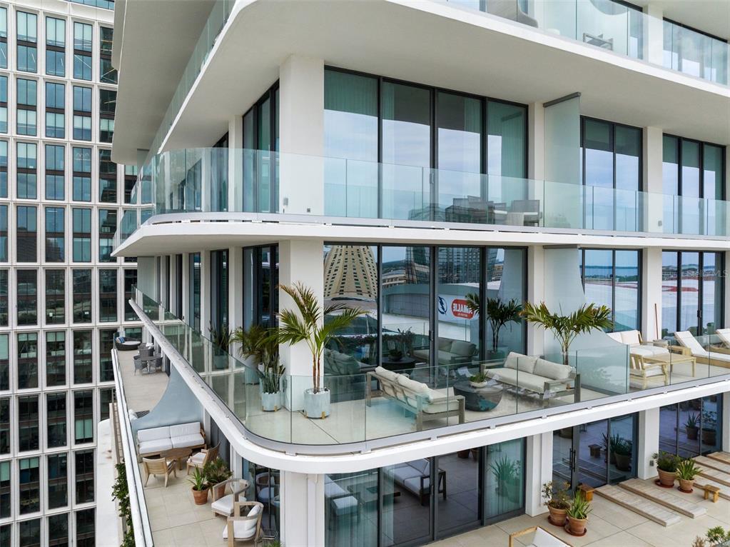 An elevated view of a modern apartment building with multiple balconies featuring glass railings and furniture — 1000 WATER STREET UNIT 1103, TAMPA, FL
