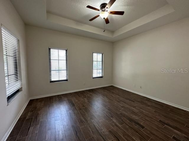 An empty room features wood-look tile flooring, a tray ceiling with a fan, and two windows — 906 PAWSTAND ROAD, CELEBRATION, FL