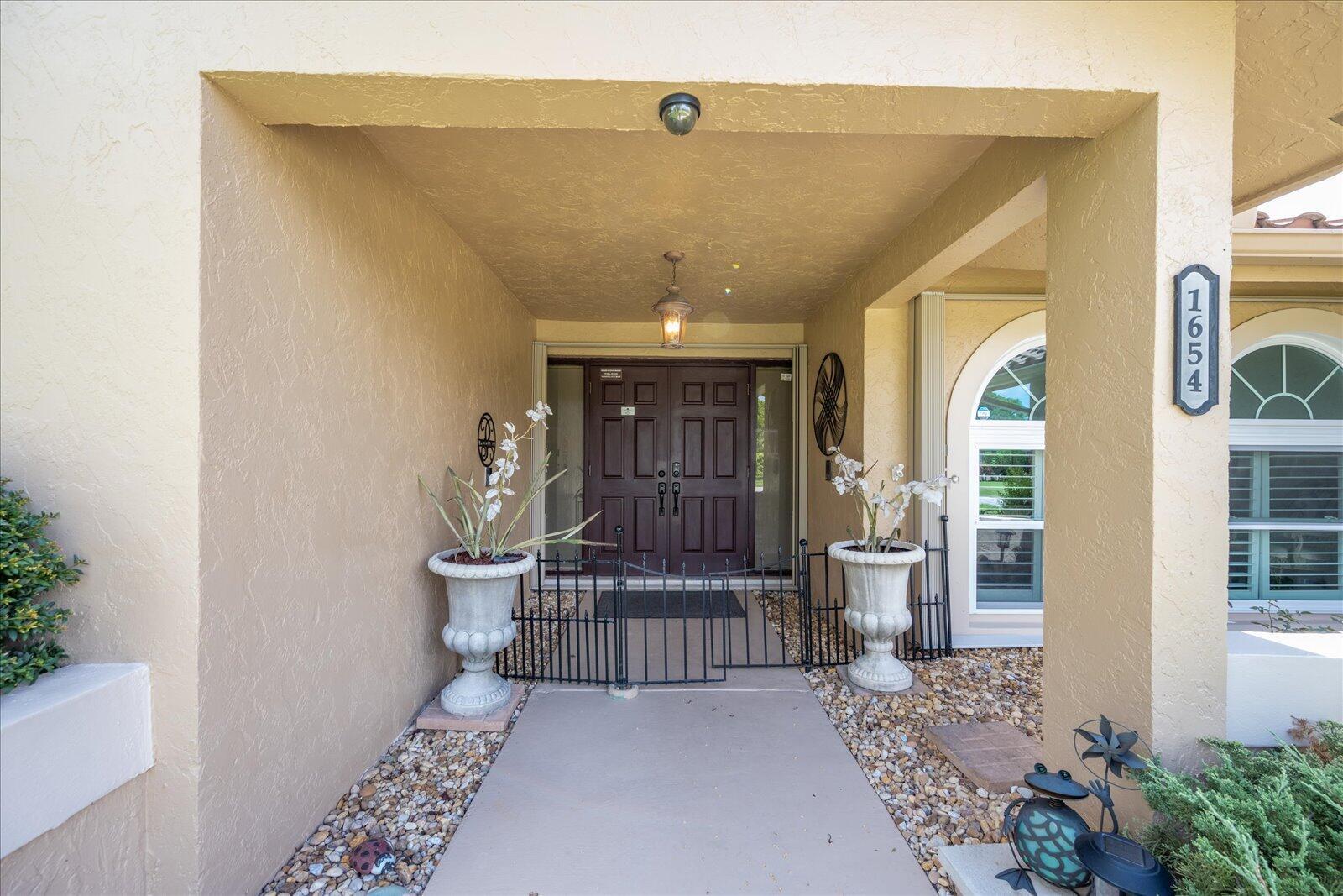 A covered entryway features a dark brown double door, two large planters, and a metal gate — 1654 Farmington Circle, Wellington FL 33414, WELLINGTON, FL