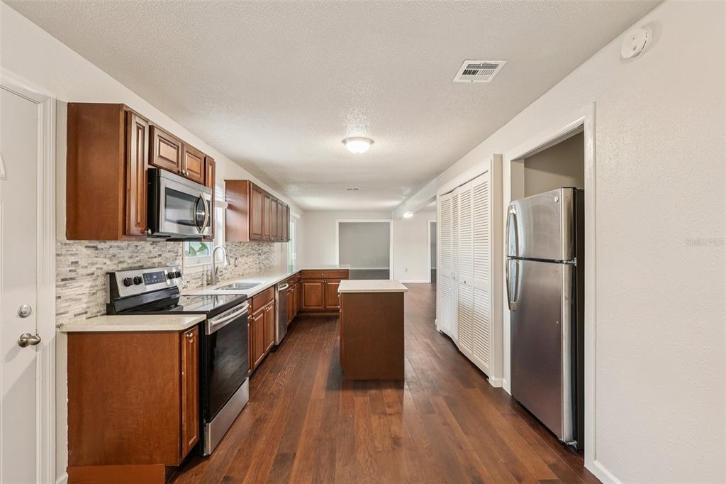 A kitchen with wood cabinets, stainless steel appliances, a small island, and dark wood flooring — 104 HALLMARK COURT, LAKE MARY, FL