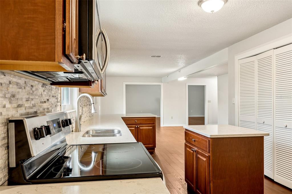A kitchen features wood cabinets, white countertops, a stone backsplash, and a small island — 104 HALLMARK COURT, LAKE MARY, FL