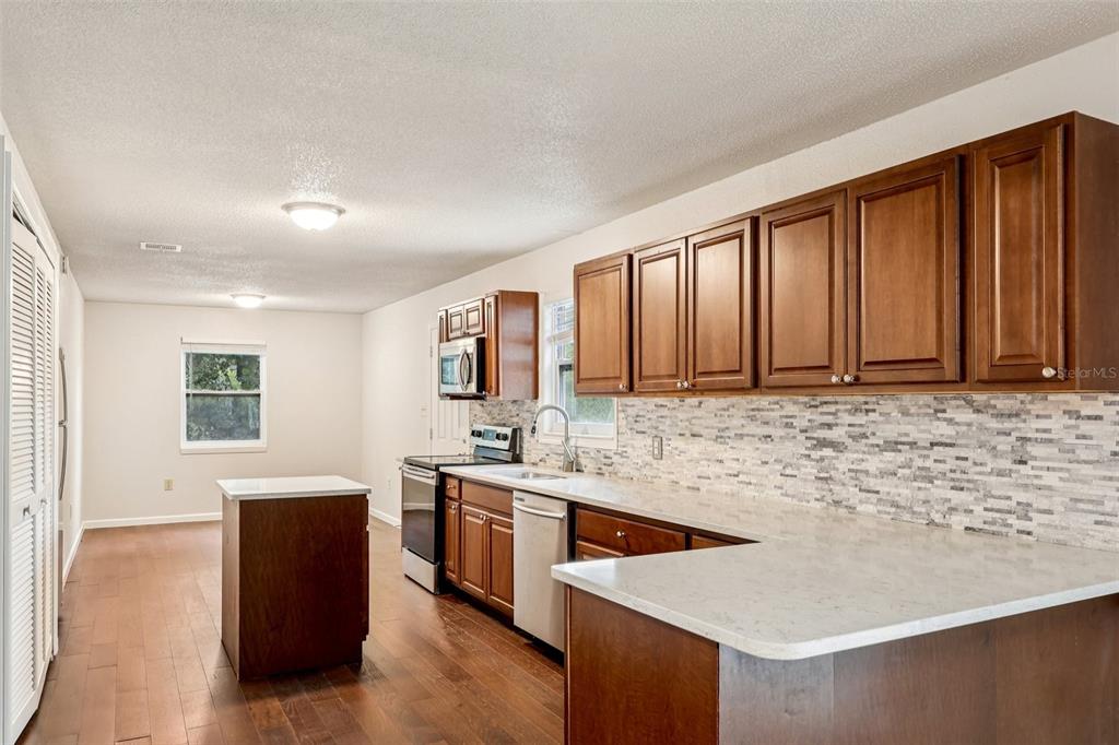 A kitchen with wood cabinets, stone-look backsplash, white countertops, and a small center island — 104 HALLMARK COURT, LAKE MARY, FL