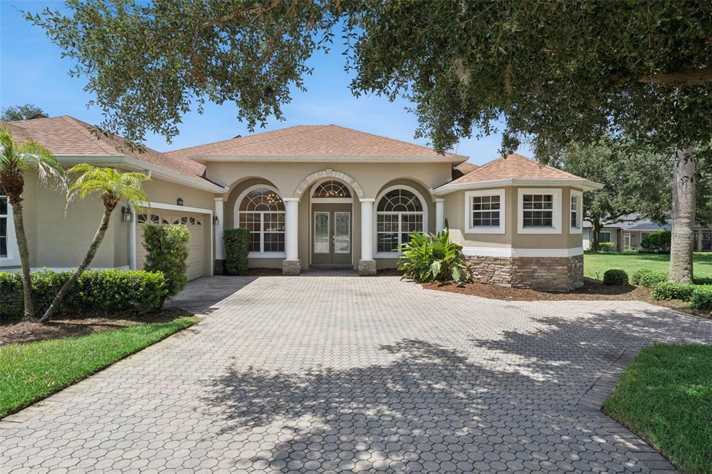 A single-story house with a paved driveway, arched entryway, and stone accents on the exterior — 1353 BRIDGE HILL LANE, CLERMONT, FL