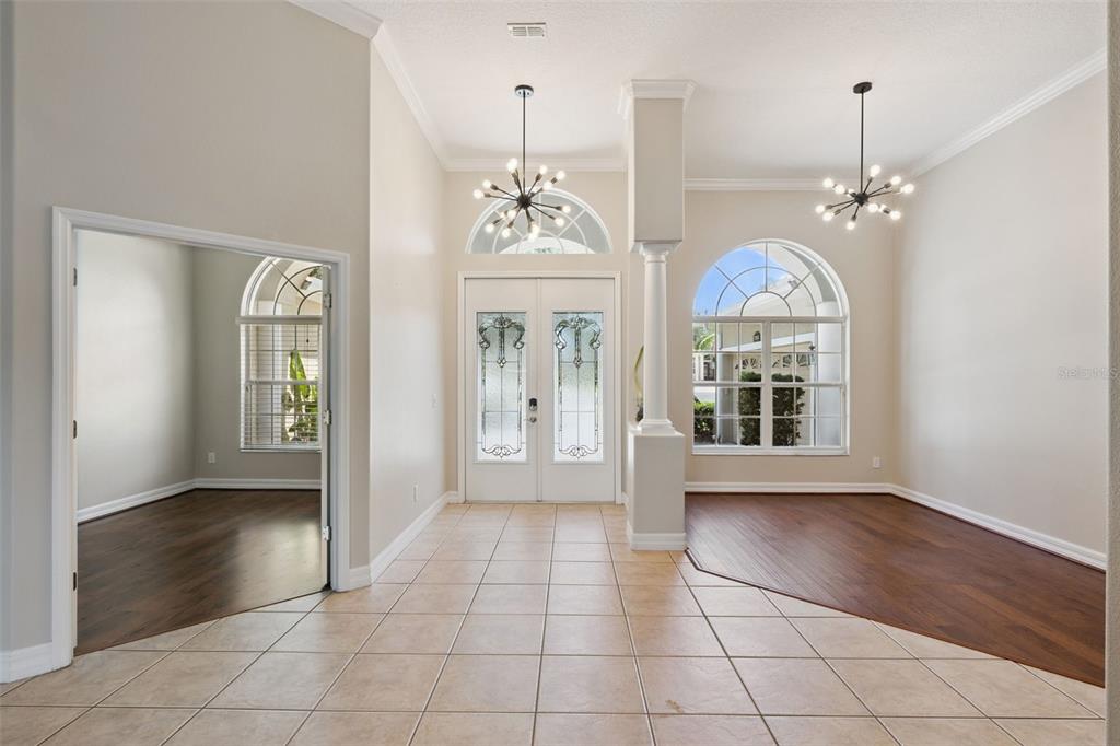 A bright entryway features tile flooring, a central column, two chandeliers, and arched windows — 1353 BRIDGE HILL LANE, CLERMONT, FL