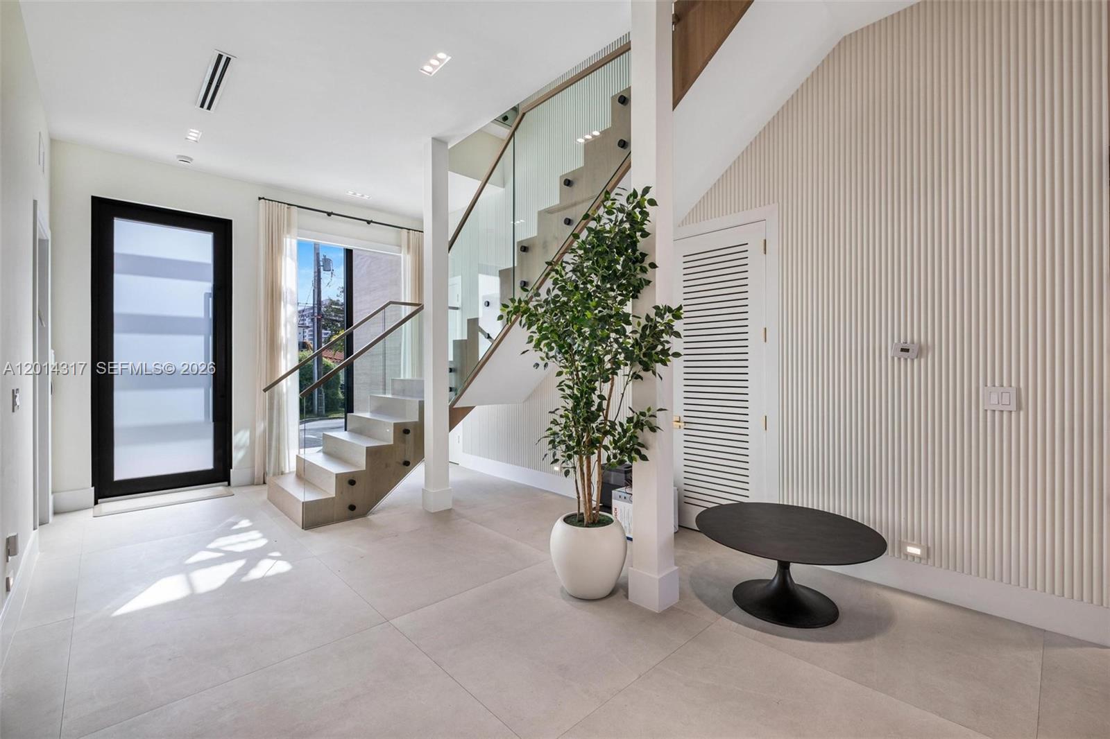 A modern entryway features light tile floors, a glass-railed staircase, and a textured accent wall — 9280 Byron Ave, Surfside FL 33154, SURFSIDE, FL
