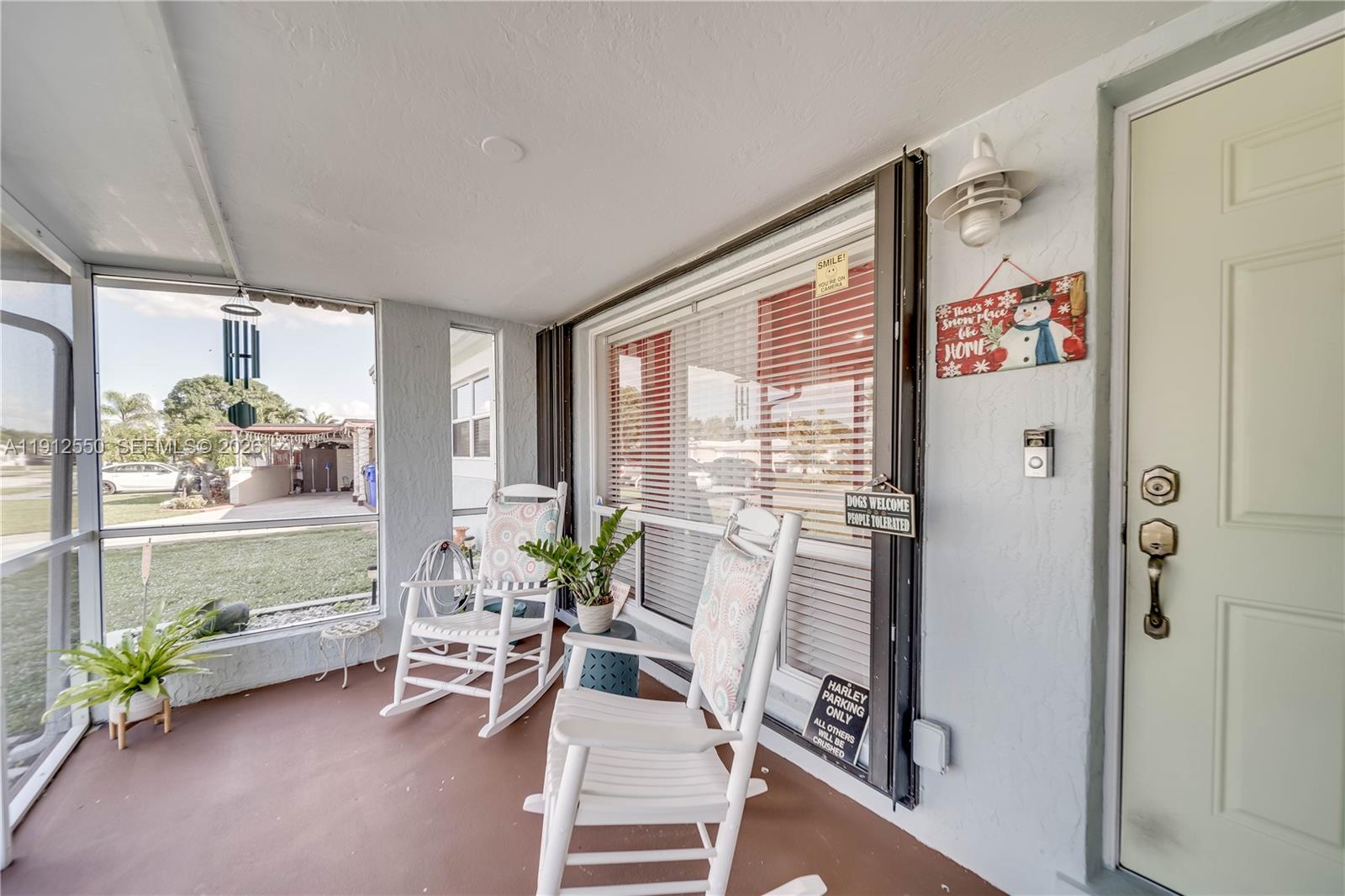 A screened-in porch features white rocking chairs, a brown floor, and views of a neighborhood — 7440 Fillmore St, Hollywood FL 33024, HOLLYWOOD, FL