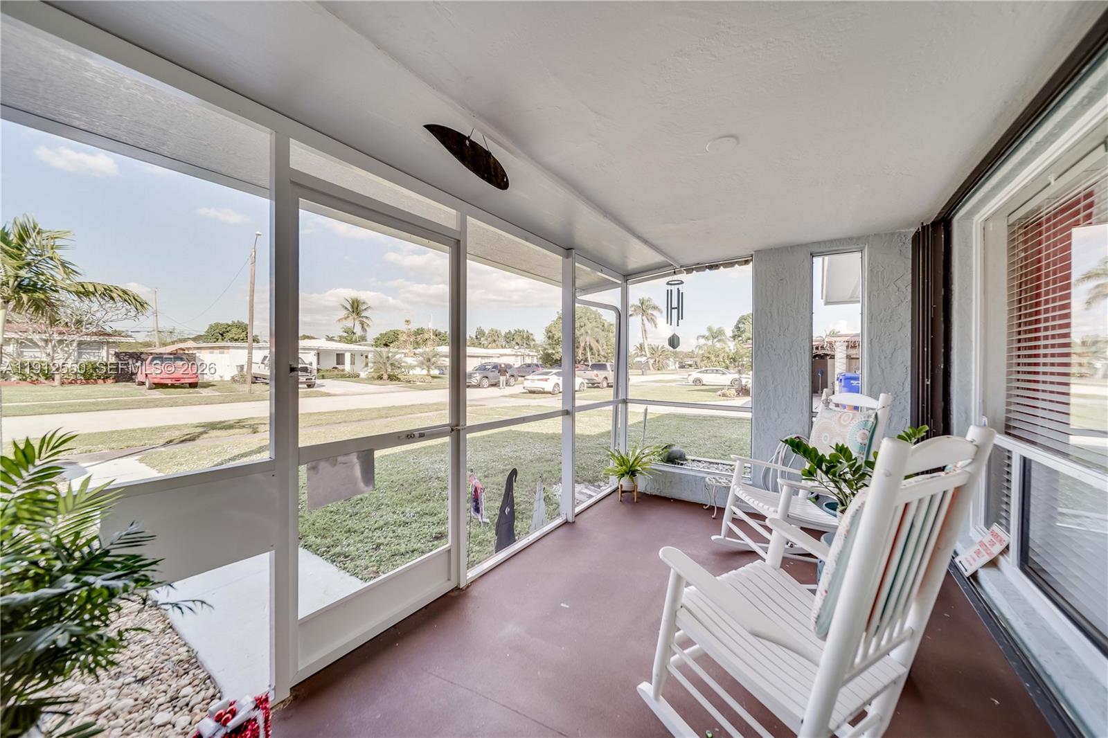 A screened-in porch features a white rocking chair, tiled flooring, and views of a neighborhood — 7440 Fillmore St, Hollywood FL 33024, HOLLYWOOD, FL
