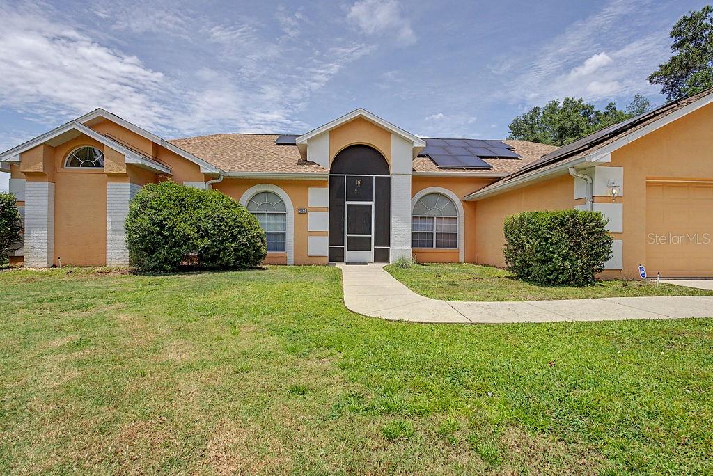 A single-story house with a tan stucco exterior, arched entryway, and solar panels on the roof — 20811 SW 81ST LOOP, DUNNELLON, FL