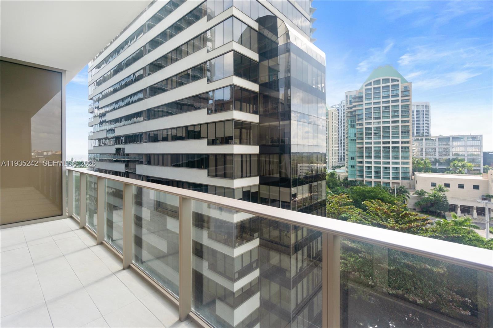 A balcony with a glass railing overlooks a modern high-rise building and city skyline — 2678 Tigertail Ave # 715, Miami FL 33133, MIAMI, FL