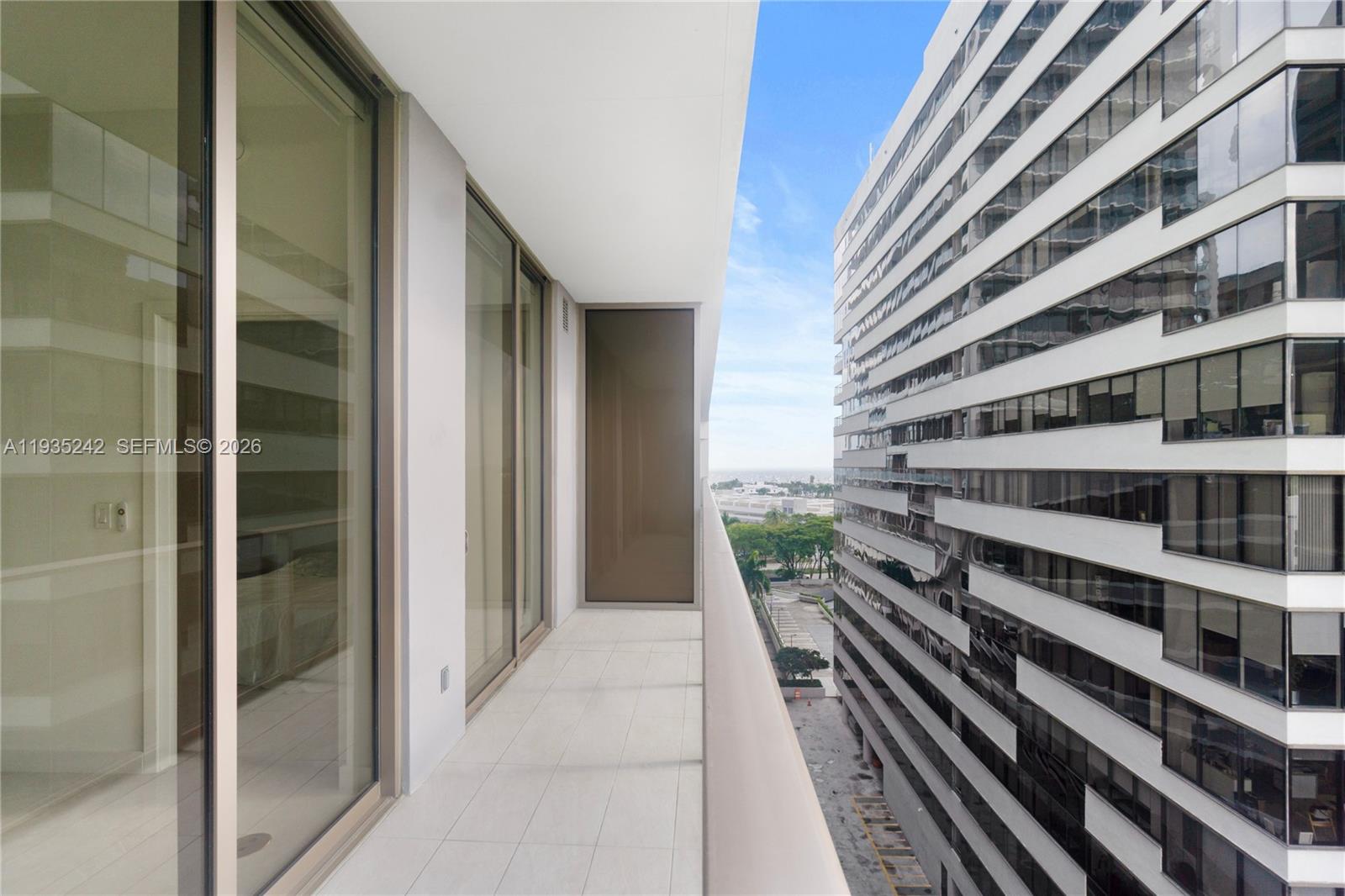 A narrow balcony with white tile flooring overlooks a street and a neighboring high-rise building — 2678 Tigertail Ave # 715, Miami FL 33133, MIAMI, FL