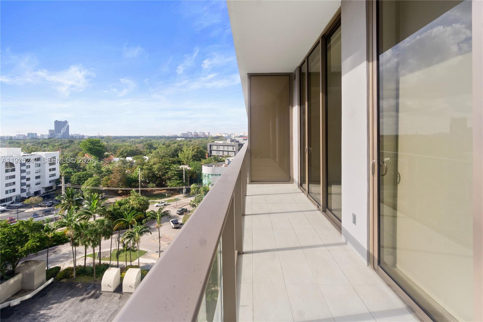 A high-rise balcony features light tile flooring, a glass railing, and views of trees and buildings — 2678 Tigertail Ave # 715, Miami FL 33133, MIAMI, FL