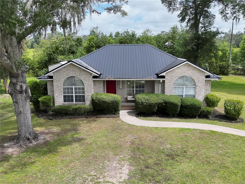 A single-story brick house with a dark metal roof and a red front door — 1302 MAYRA ROAD SW, LIVE OAK, FL