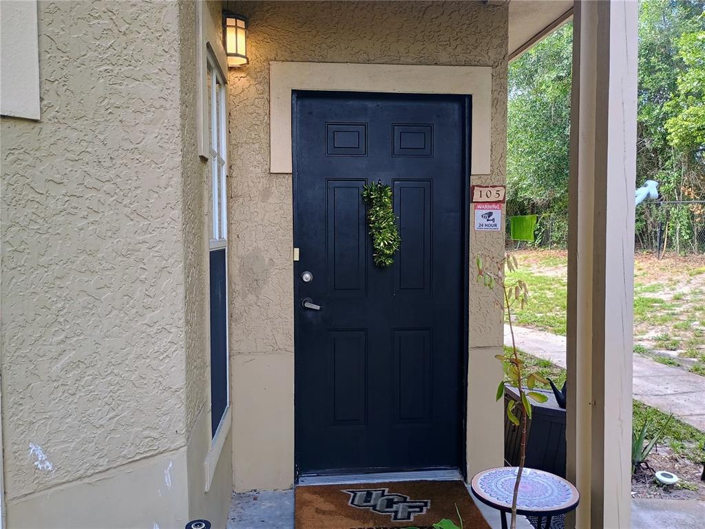 A black front door with a wreath and a UCF doormat under a porch light — 143 VILLA DI ESTE TERRACE UNIT 105, LAKE MARY, FL