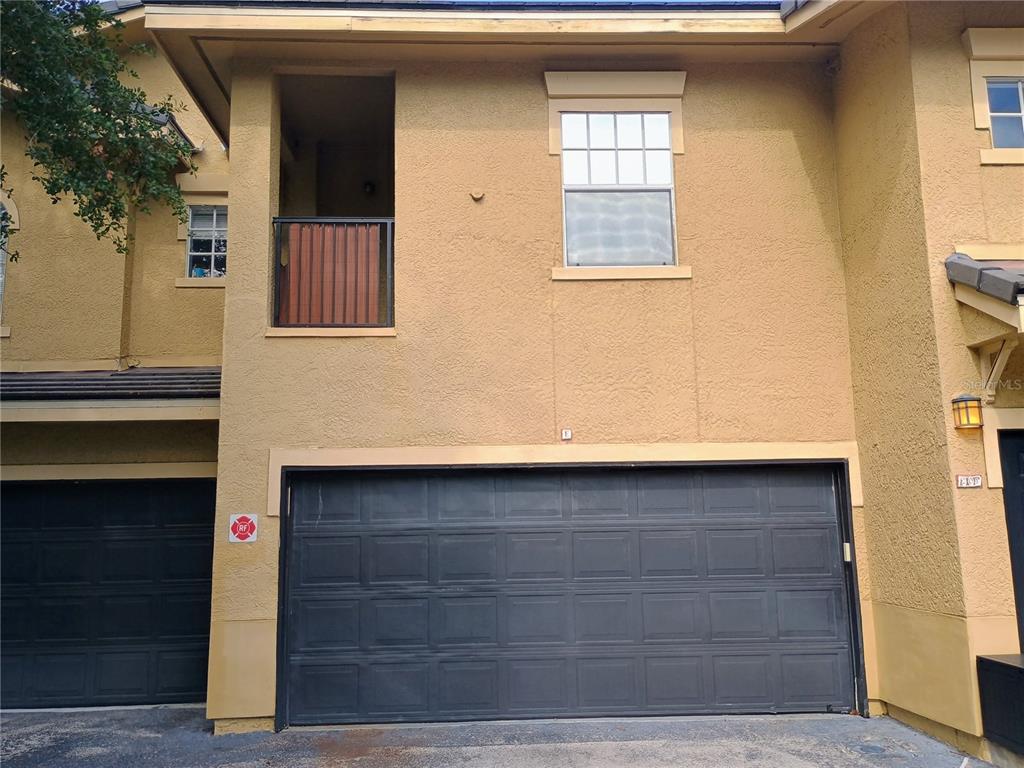 A two-story building exterior features a dark garage door, a balcony, and a window — 143 VILLA DI ESTE TERRACE UNIT 105, LAKE MARY, FL