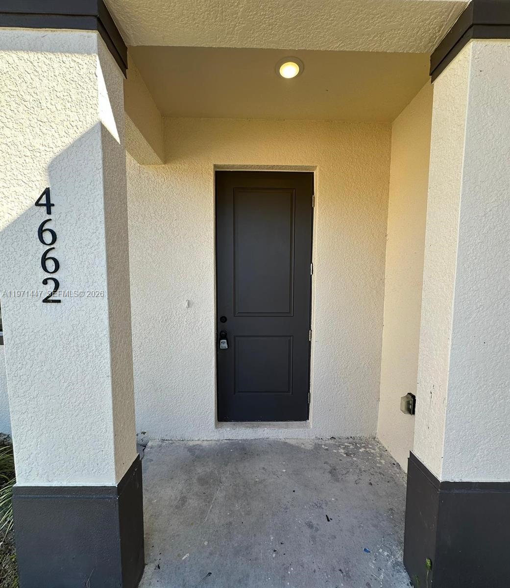 A dark front door is set within a covered entryway with light-colored stucco walls — 4662 SW 26th st # 4662, Lehigh Acres FL 33973, LEHIGH ACRES, FL