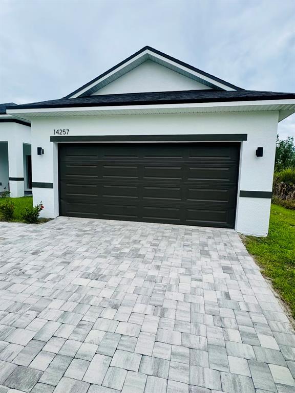 A white house exterior features a dark garage door and a gray paver driveway — 14257 IMLAY AVENUE, PORT CHARLOTTE, FL