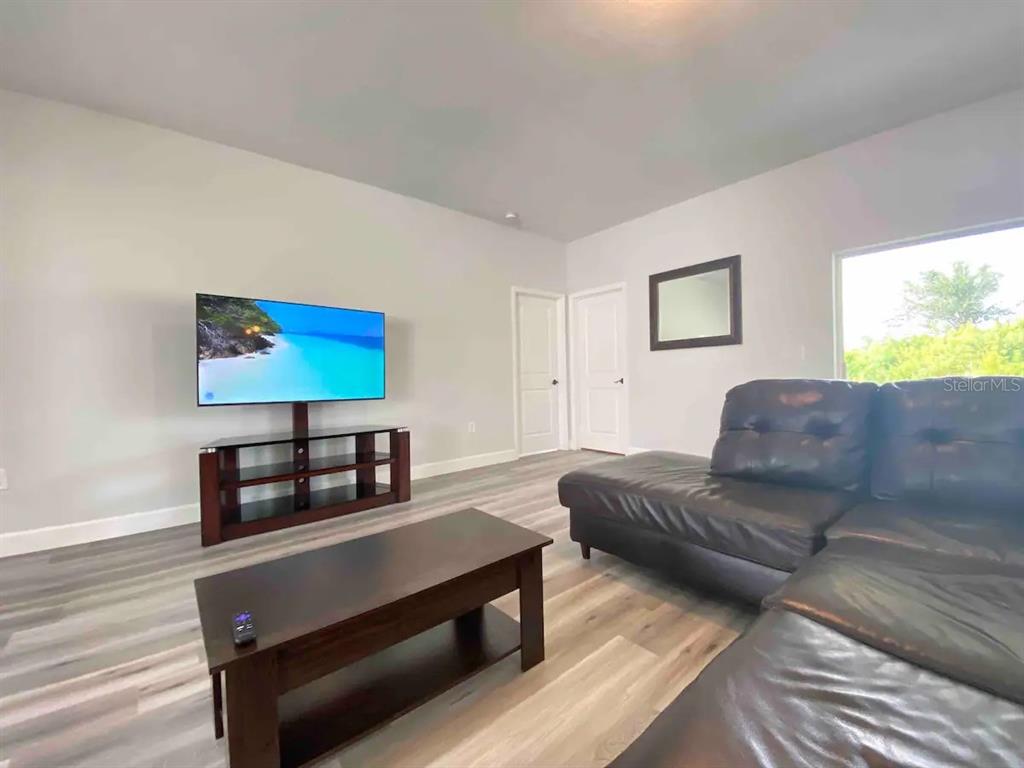 A living room features light gray walls, wood-look flooring, a television, and a leather sectional — 14257 IMLAY AVENUE, PORT CHARLOTTE, FL