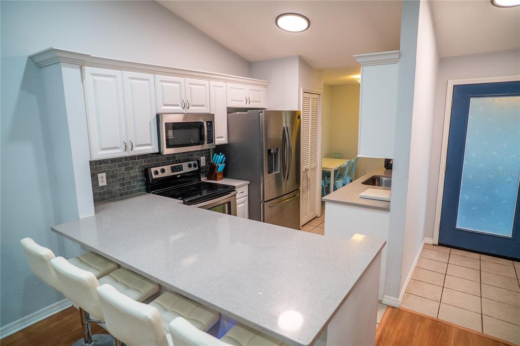 A kitchen with white cabinets, stainless steel appliances, and a gray quartz breakfast bar — 7802 RICHWOOD DRIVE, ORLANDO, FL